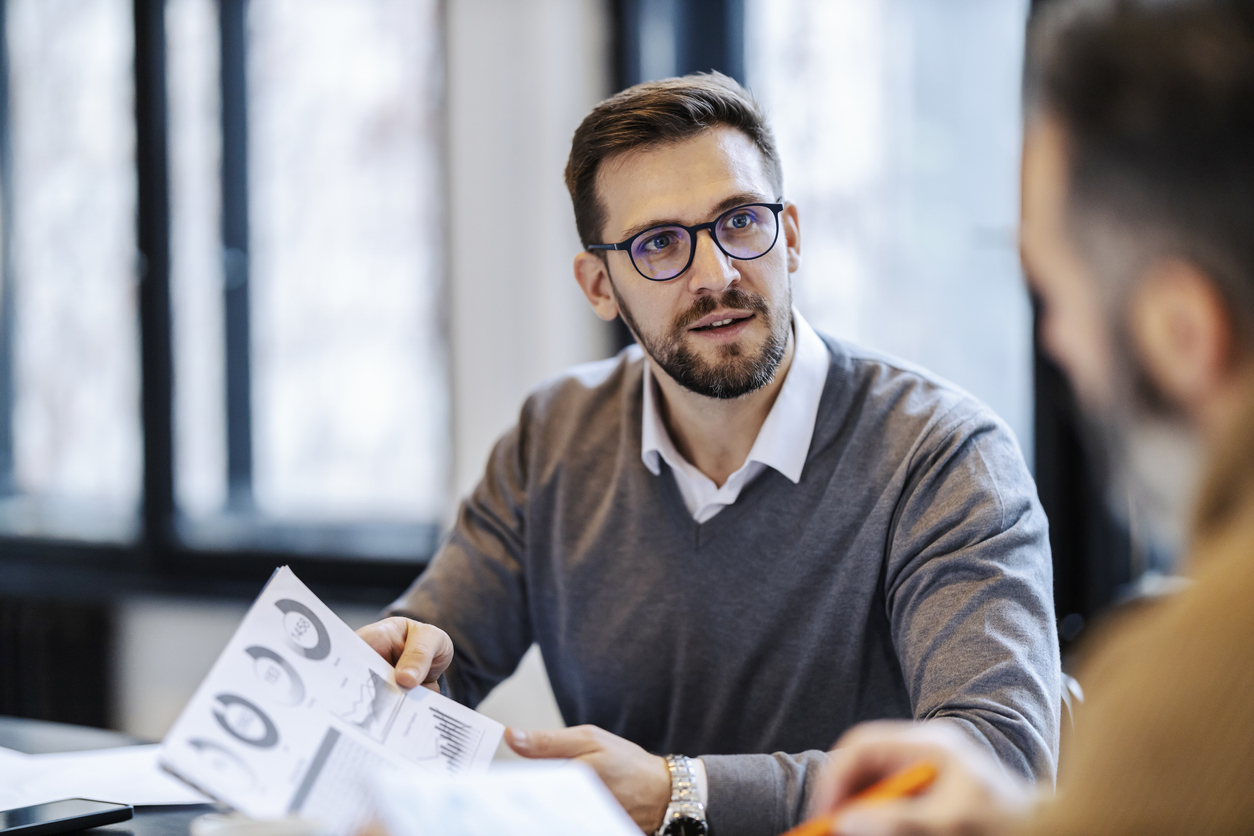 a-businessman-is-holding-document-with-charts-and-statistics-and-discussing-with-colleague-on-a-business-meeting-in-boardroom